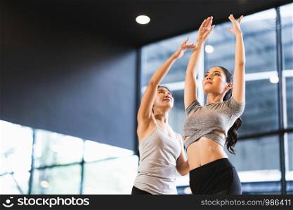 Beautiful Asian woman learning yoga pose with female instructor in yoga studio or health club. Sport exercise activity, gymnastics or ballet dancing class, or healthy people lifestyle concept