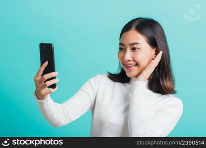 Beautiful Asian woman smile she using a smartphone to selfie photo, happy female photography by mobile phone on mobile phone isolated on a blue background, Technology concept