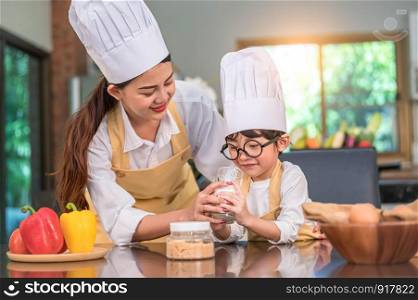 Beautiful Asian woman teaching cute little boy with eyeglasses to drink milk in kitchen at home together. Lifestyles and Family. Son dislike milk and doing funny face with milk glass. Food and drink