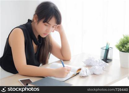 Beautiful asian woman tired and stressed with writing overworked at desk, girl with worried not idea with notebook and crumpled paper at office, freelance and business concept.