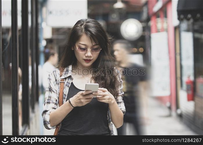 beautiful asian woman walking on urban street and connecting on smart phone