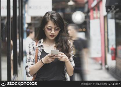 beautiful asian woman walking on urban street and connecting on smart phone