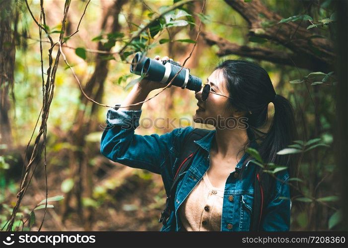 Beautiful Asian woman with binoculars telescope in forest looking destination. People lifestyles and leisure activity. Nature and backpacker traveling jungle background. Bird watching and living