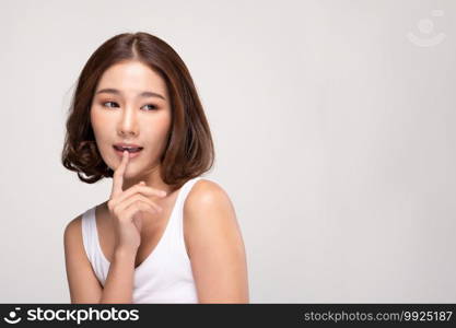 Beautiful Asian woman with short hair looking at camera making surprise and quiet sign forefinger touch on lips with clean and fresh skin,isolated on gray background,Beauty and Cosmetics Concept