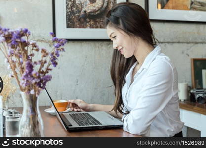 Beautiful Asian woman working with laptop and drinking coffee