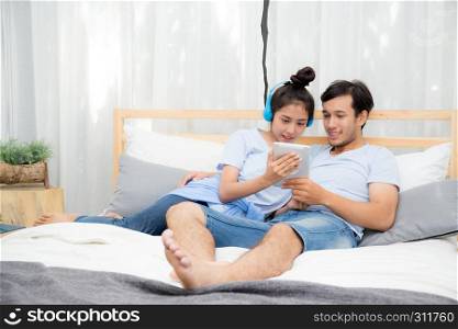 Beautiful asian young couple listening to music with tablet on bed, Love, dating,Young couple in sitting together in bed using a Tablet.