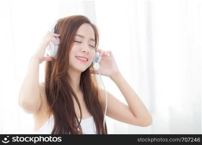 Beautiful asian young woman enjoy listen music with headphone while sitting in bedroom, relax girl with earphone internet online, leisure and technology concept.