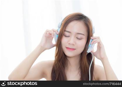 Beautiful asian young woman enjoy listen music with headphone while sitting in bedroom, relax girl with earphone internet online, leisure and technology concept.
