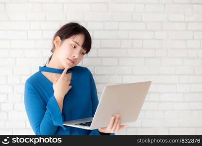 Beautiful asian young woman hipster using working laptop thinking idea on cement concrete background, girl doubt and question with computer internet online, freelance and business concept.