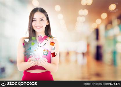 Beautiful asian young woman in red dress holding shopping cart with icon product on blur bokeh background, ecommerce shopping online concept.