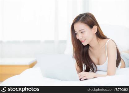 Beautiful asian young woman lying on bed using laptop at bedroom for leisure and relax, freelance with girl working notebook, communication concept.