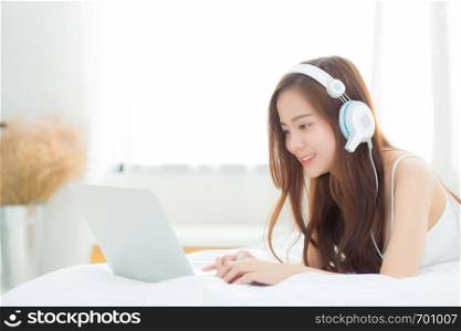 Beautiful asian young woman relax listening to music with headphone and laptop online internet on vacation in bedroom, cheerful of asia girl leisure, lifestyle concept.