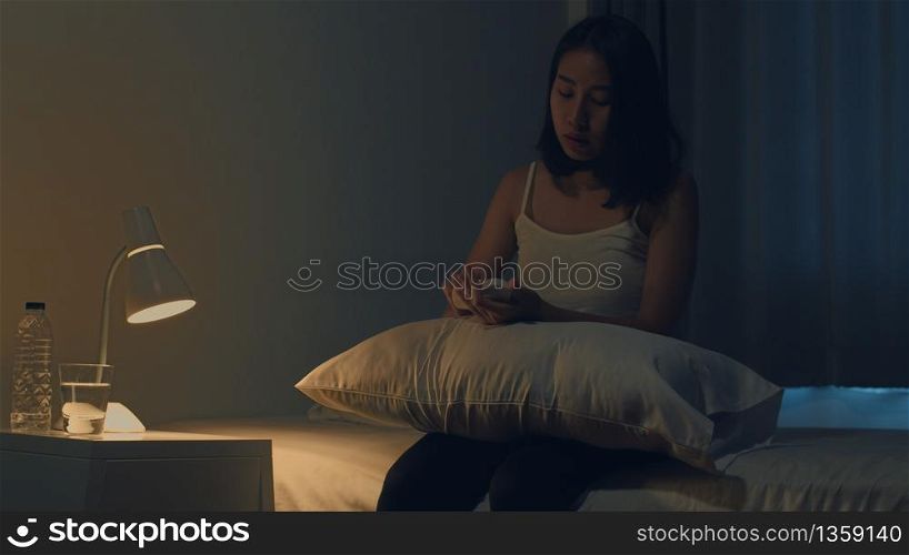 Beautiful Asian young woman sitting on bed take sleeping pill or night medicine in bedroom. Unhealthy sick Indian female suffers from insomnia or headache, depressed girl holds antidepressant meds.