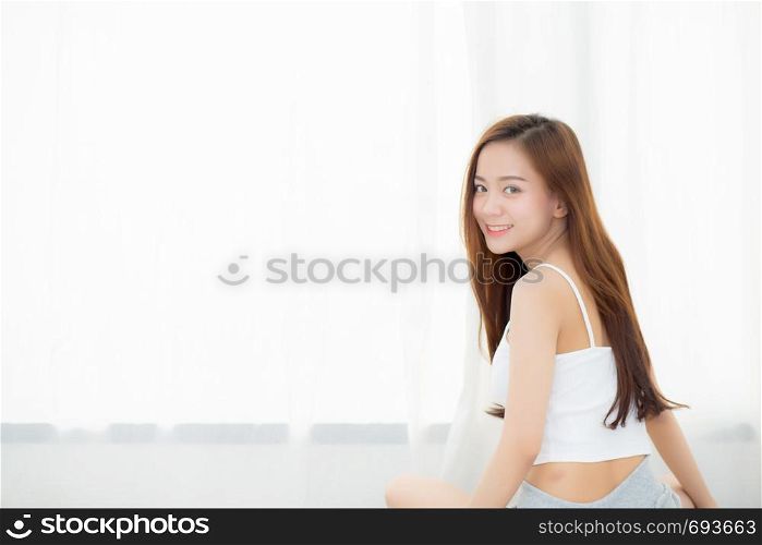 Beautiful asian young woman smiling with happiness leisure sitting on bed at home by the window, girl relax and wellness concept.