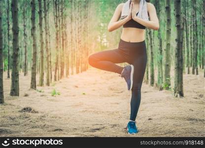 Beautiful Asian young woman standing and doing yoga in forest. Exercise and meditation concept. Pay obeisance or raise hand concept. Pine wood in summer theme. Front view
