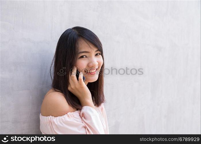 Beautiful asian young woman talking on Mobile Phone, over concrete wall