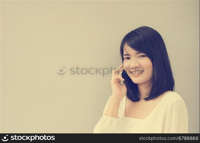 Beautiful asian young woman talking on Mobile Phone over concrete wall, vintage filtered image.
