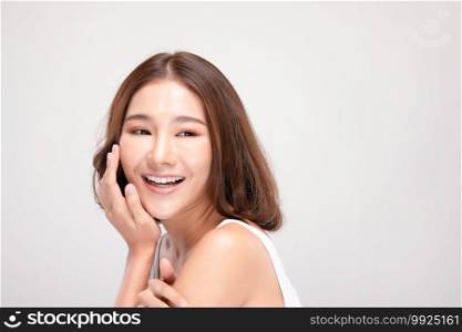 Beautiful Asian young woman touching soft cheek smile with clean and fresh skin Happiness and cheerful with positive emotional,isolated on gray background,Beauty and Cosmetics Concept