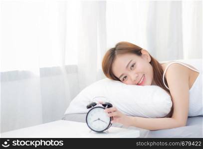 Beautiful asian young woman turn off alarm clock in morning, wake up for sleep with alarm clock, relax and lifestyle concept.