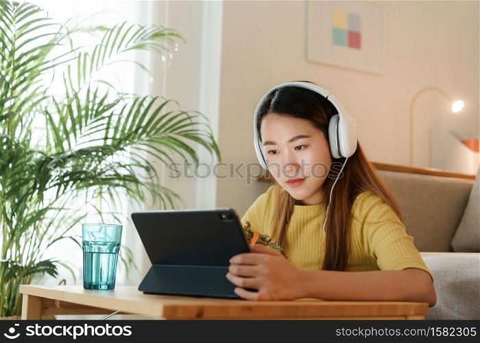 beautiful Asian young woman using a tablet and eat salad for lunch on table work at home. concept working from home