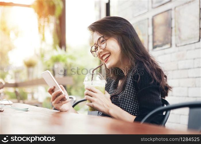 beautiful asian younger woman drinking cool green tea in bottle and looking on mobilephone screen with happiness face