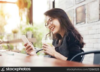 beautiful asian younger woman drinking cool green tea in bottle and looking on mobilephone screen with happiness face