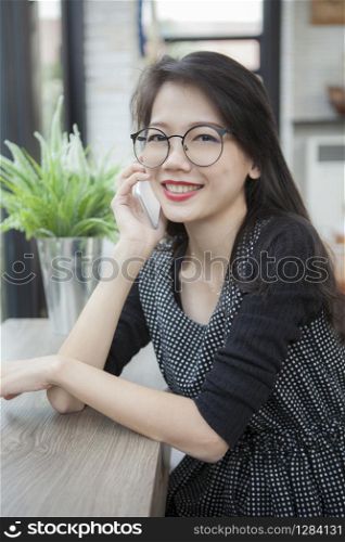 beautiful asian younger woman talking on smart phone with toothy smiling face at home