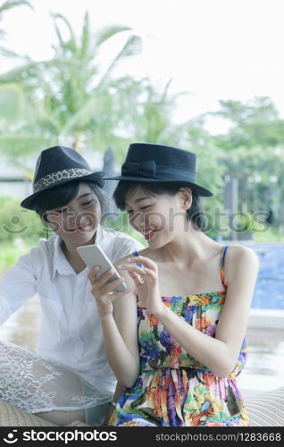 beautiful asian younger woman toothy smiling face and playing on smart phone screen