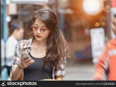 beautiful asian younger woman using smart phone while walking in city shopping area