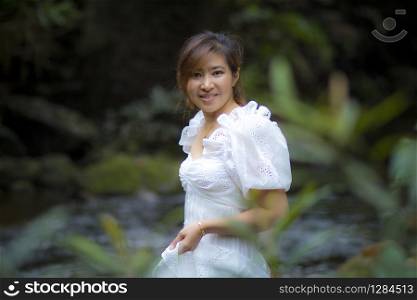 beautiful asian younger woman wearing white dress standing in green natural background