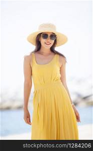 beautiful asian younger woman wearing yellow dress relaxing on summer vacaiton beach