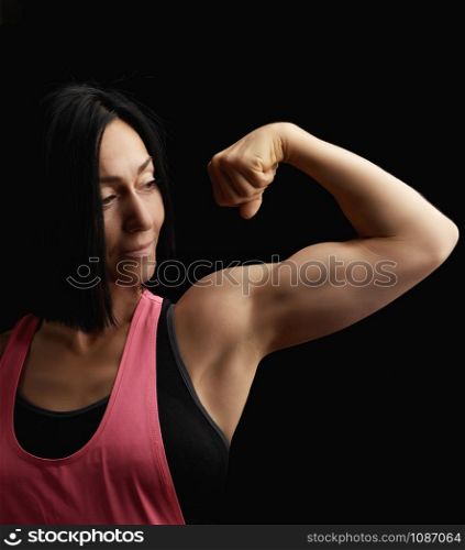 beautiful athletic girl raised and bent her arm demonstrating her biceps, athlete is standing on a dark background, wearing a black top