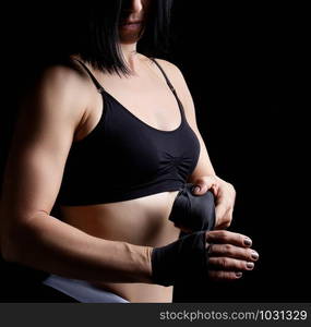 beautiful athletic girl with black hair rewinds her hand with a black elastic bandage before training, dark background