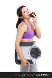 Beautiful athletic woman eating an apple and holding a scale, isolated on white