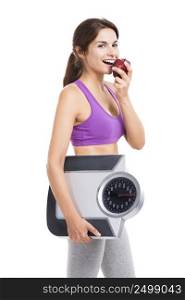 Beautiful athletic woman eating an apple and holding a scale, isolated on white