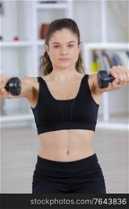 beautiful athletic woman pumping up muscules with dumbbells in gym
