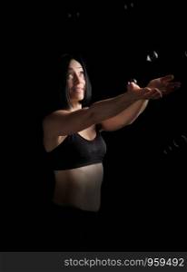 beautiful athletic woman with muscular body dressed with a black topic catches soap bubbles on a black background, studio portraits in a low key