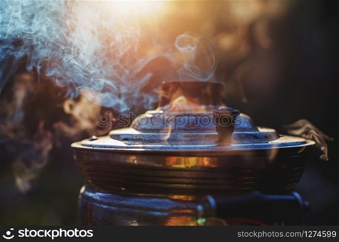 Beautiful atmospheric smoke and mist rising from an old samovar with setting sun on background