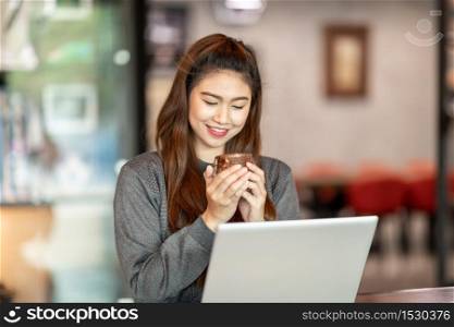 Beautiful Attractive Asian Business woman smile and holding coffee in Coffee shop cafe with computer laptop on the table feeling so happiness and comfortable,Warm Tone