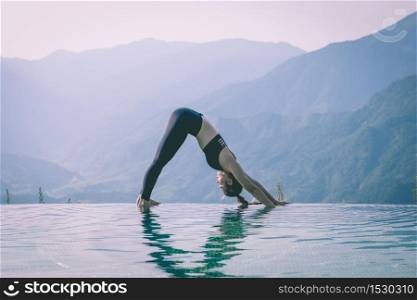 Beautiful Attractive Asian woman practice yoga Downward Facing Dog or Adho Mukha Svanasana pose on the pool above the Mountain peak in the morning in front of beautiful nature views in SAPA vietnam