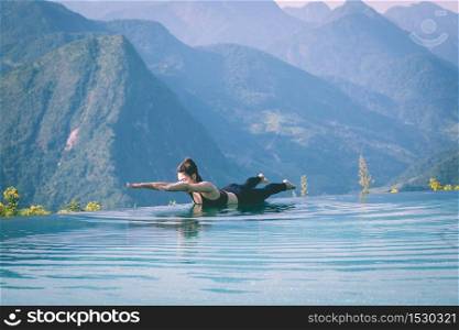 Beautiful Attractive Asian woman practice yoga Locust or Shalabhasana pose on the pool above the Mountain peak in the morning in front of beautiful nature views in SAPA vietnam