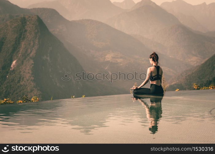 Beautiful Attractive Asian woman practice yoga Lotus pose on the pool above the Mountain peak in the morning in front of beautiful nature views,Feel so comfortable and relax in holiday,Warm Tone