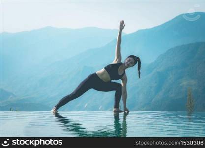 Beautiful Attractive Asian woman practice yoga Triangle pose or Utthita Trikonasana pose on the pool above the Mountain peak in the morning in front of beautiful nature views in SAPA vietnam