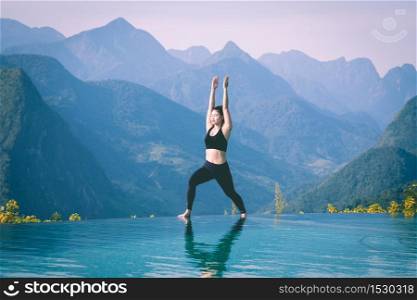 Beautiful Attractive Asian woman practice yoga Warrior I or Virabhadrasana Pose on the pool above the Mountain peak in the morning in front of beautiful nature views in SAPA vietnam