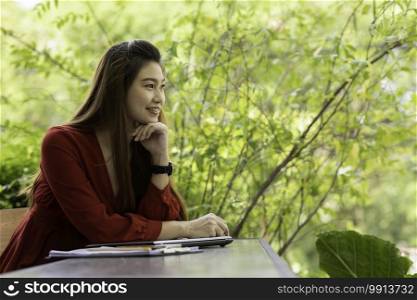 Beautiful Attractive Asian woman wearing red dress working with computer laptop looking away and thinking to get ideas and requirement in Business startup feeling so happiness,Business Startup Concept