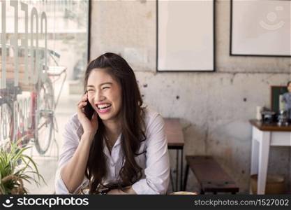 Beautiful Attractive Asian woman working with laptop smile and talking with customer in smartphone to get idea and requirement for success her job outside office in coffee shop cafe,Business Concept