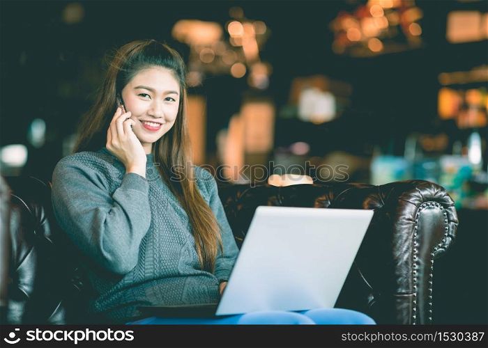 Beautiful Attractive Asian woman working with laptop smile and talking with customer in smartphone to get idea and requirement for success job outside office in coffee shop,Business Concept,Warm Tone
