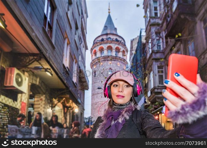 Beautiful attractive woman in headphones and cap takes selfie with view of Galata Tower on background in Istanbul,Turkey . Beautiful woman in red dress sits on a ferry Istanbul on background.