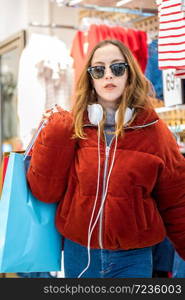 Beautiful attractive young girl in jumper and jeans with sunglasses and bags exits from shopping store