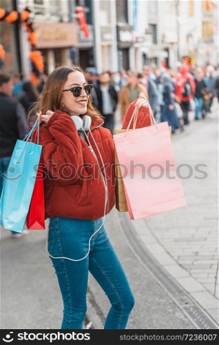 Beautiful attractive young girl in jumper and jeans with sunglasses and bags walks at a crowded street after shopping